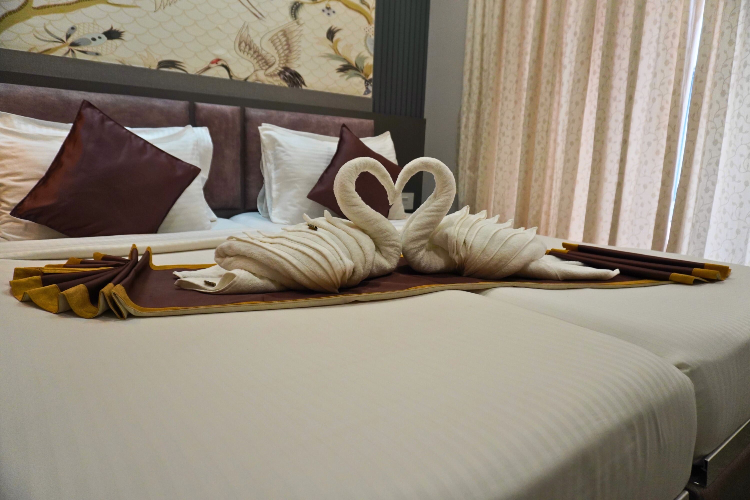 A neatly made bed with a swan towel design, pillows, and a decorative wall.