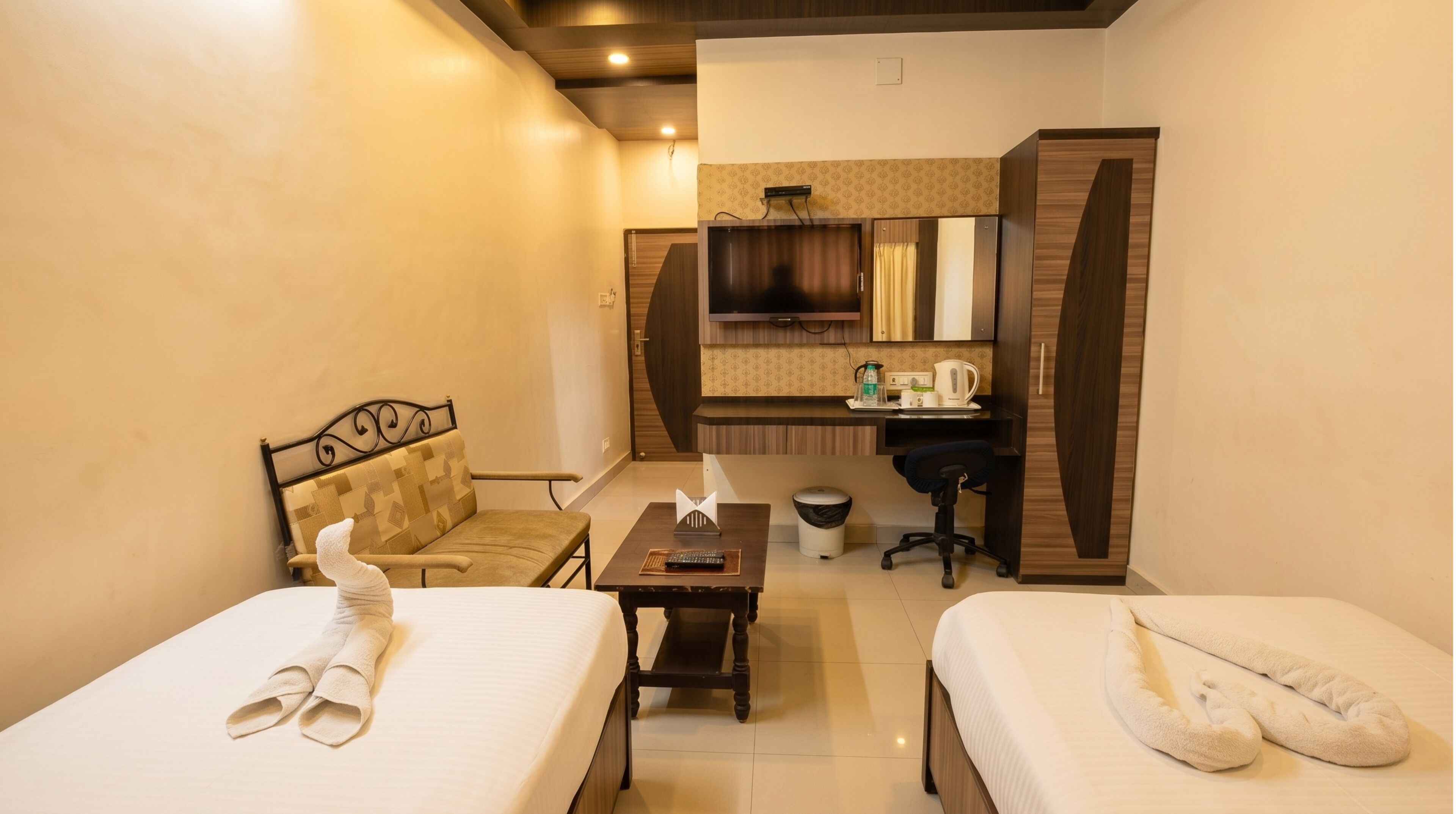 A hotel room with two beds, a desk, a chair, a TV, and a small bathroom.
