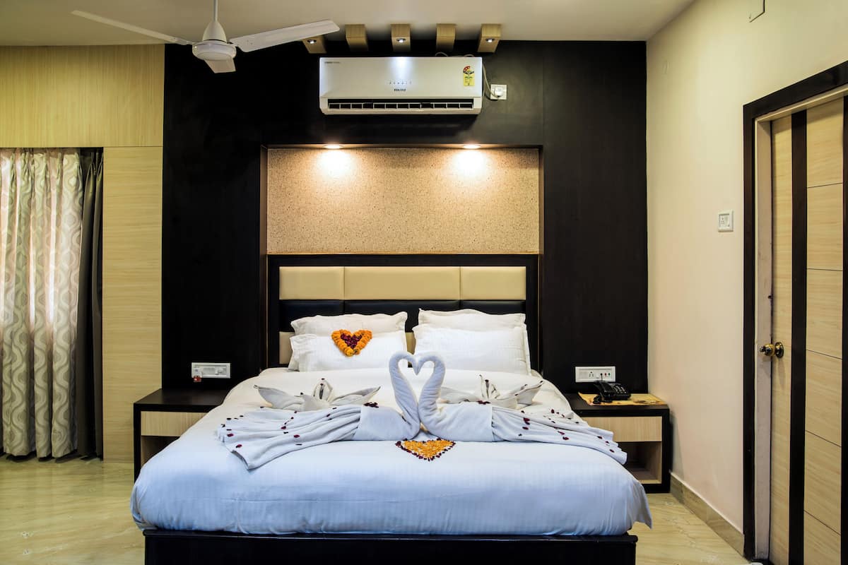 Una habitación de hotel con cama, mesita de noche, aire acondicionado, ventilador de techo y puerta.