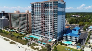 Un hotel de gran altura con múltiples balcones, una zona de piscina y vistas a la playa.