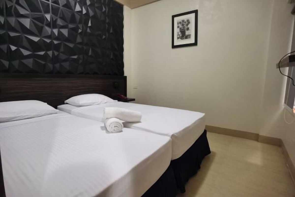 A hotel room with two beds, a dark geometric-patterned headboard, a framed picture on the wall, and a simple, clean design.