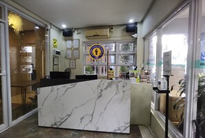 Un área de recepción con mostrador de mármol, puertas de vidrio y un letrero que indica una distancia social de 2 metros.