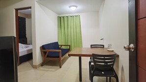 A small room with a bed, a wooden table with chairs, a green curtain, and a door. - Sunny Day Residences Cainta (Cainta)