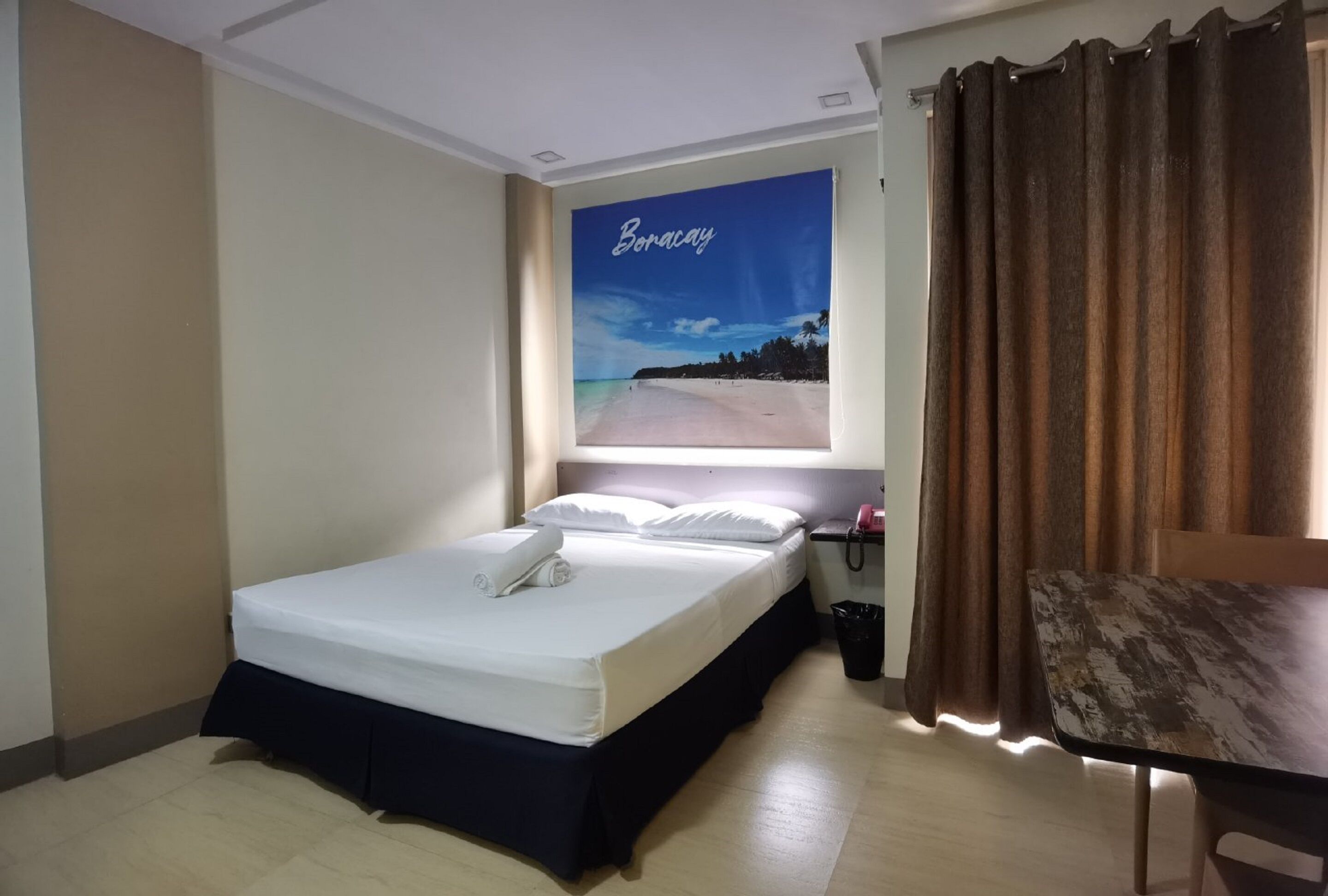 A hotel room with a bed, a nightstand, a telephone, a trash bin, and a view of Boracay.