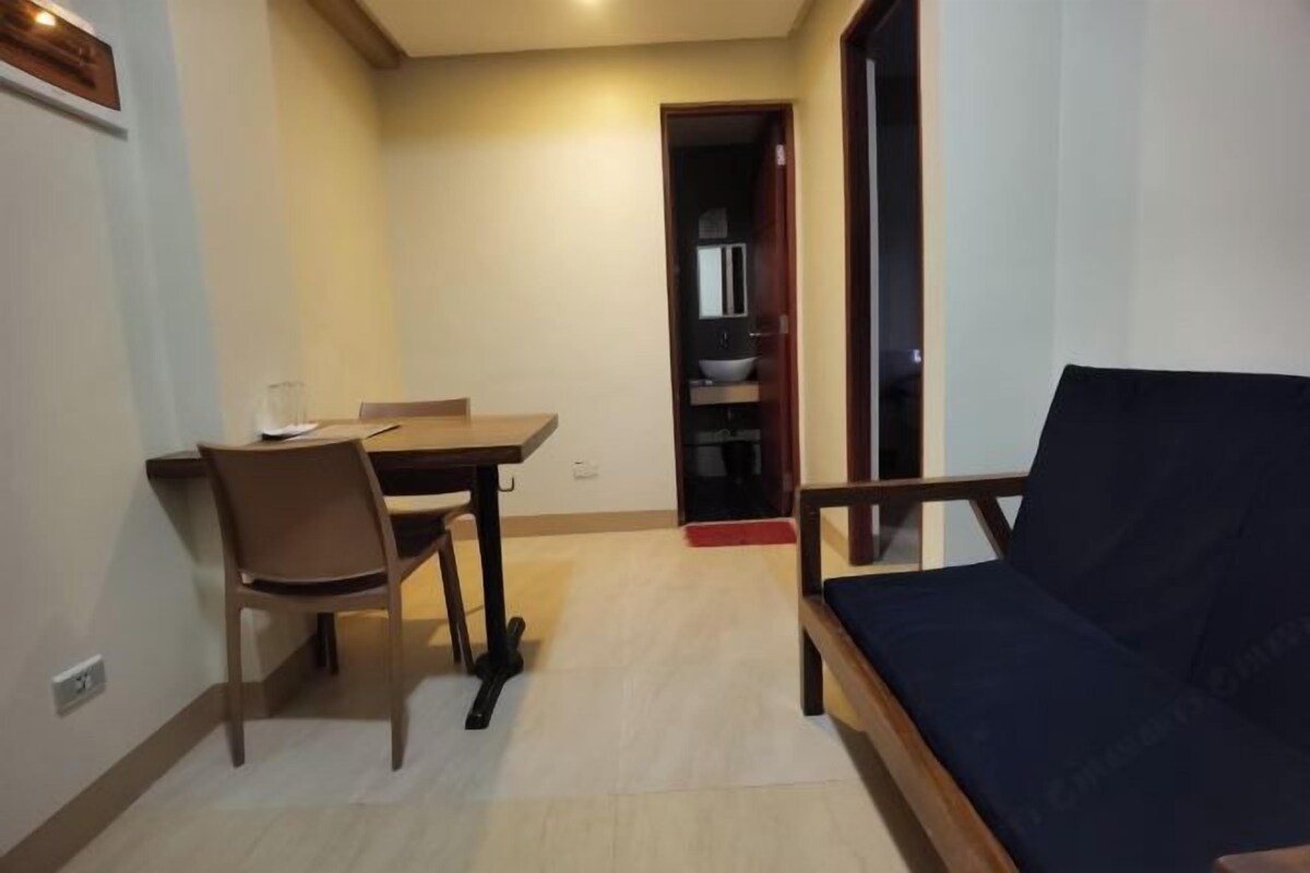 Une petite pièce comprenant un lit, une table et une chaise. Une porte donne accès à une salle de bain.
