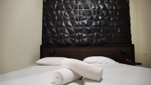 A neatly made bed with white linens and two rolled towels, a dark wooden headboard, and a geometric-patterned wall. - Sunny Day Residences Cainta (Cainta)