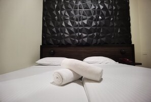 A neatly made bed with white linens and two rolled towels, a dark wooden headboard, and a geometric-patterned wall. - Sunny Day Residences Cainta (Cainta)