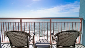 A balcony with two wicker chairs and a small table, overlooking the ocean.