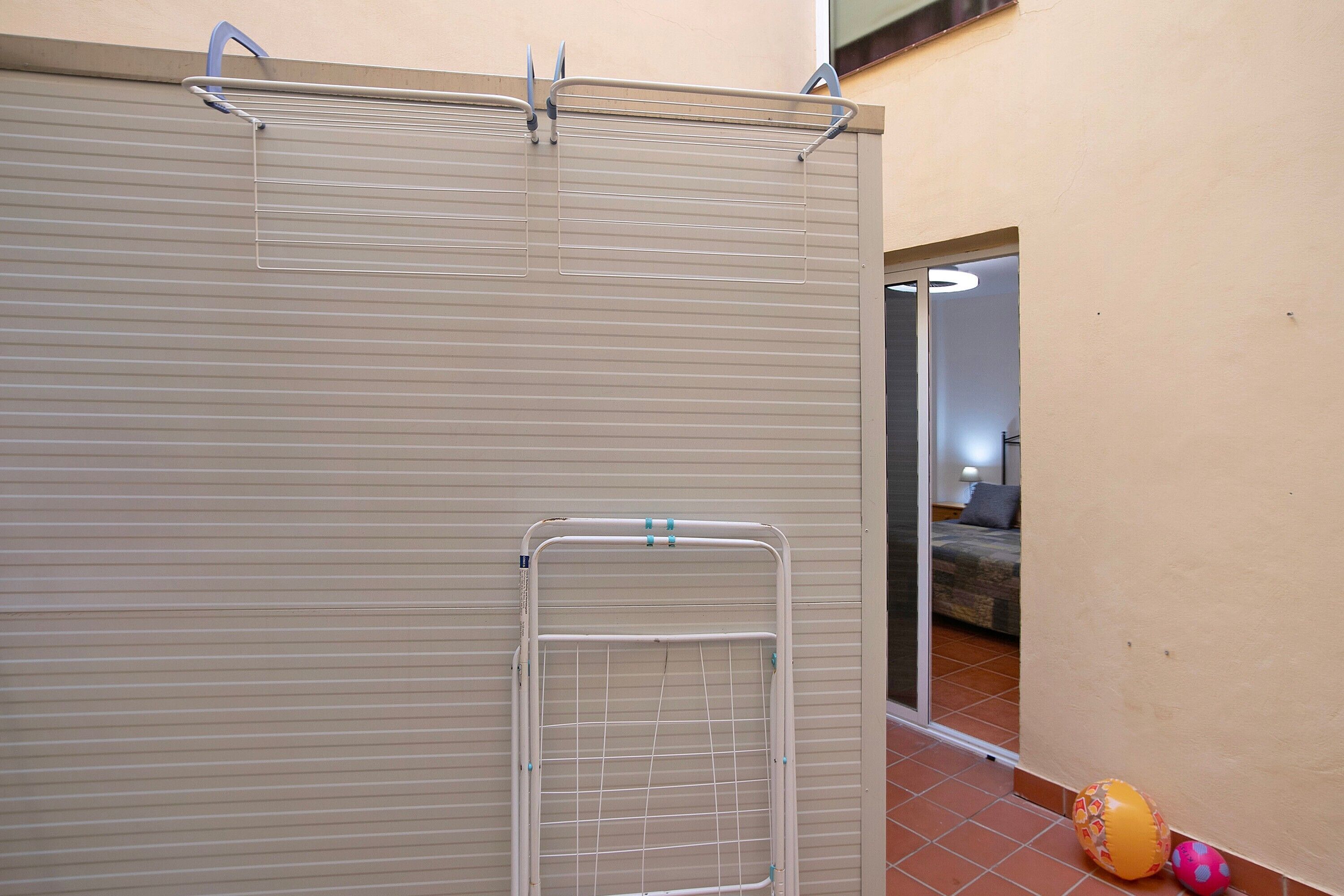 A room with a closed sliding door, a metal drying rack, and a glimpse of a bed and a wall with a circular light fixture.