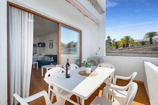 Un balcon avec une table à manger, des chaises, une bouteille de vin et une plante en pot.