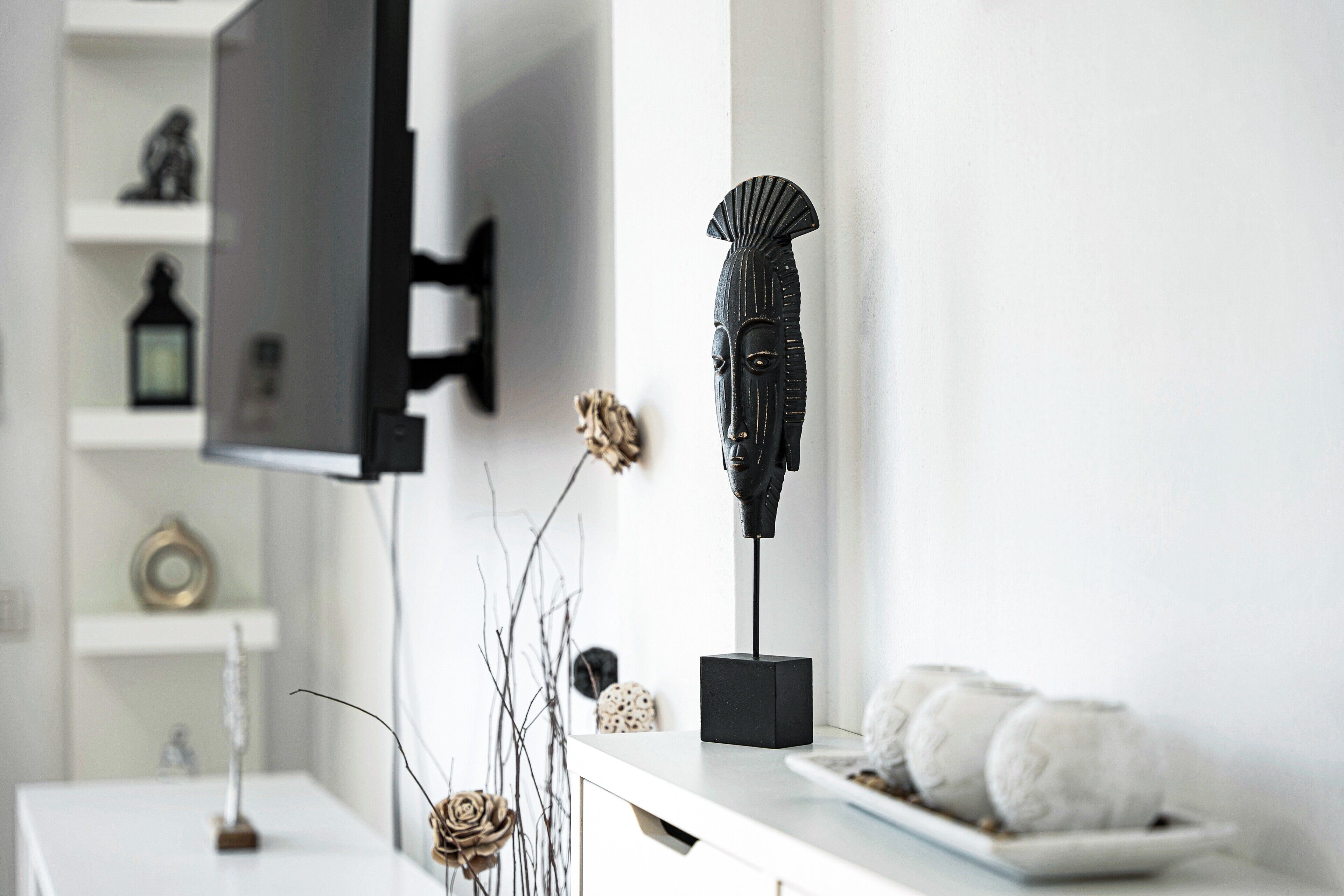 A modern interior with a flat-screen TV mounted on a wall, a decorative black sculpture on a white table, and a white plate with rolled towels.