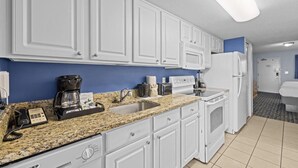 A kitchen with white cabinets, a granite countertop, a coffee maker, a sink, and a refrigerator.