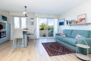 Un salon moderne avec un canapé, un coin repas avec des chaises, une cuisine équipée d’armoires et un balcon avec vue.