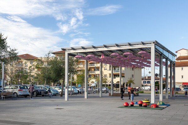 Un espace extérieur aménagé avec des parasols, une place pavée et des voitures garées.