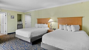 Habitación de hotel con dos camas, un escritorio con lámpara, microondas y una puerta.