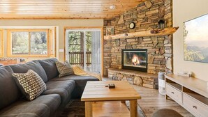 A cozy living room with a stone fireplace, a sofa, a coffee table, and a TV. - * Snowy Evening Lodge * / Treetop Views & Firepit (Big Bear)