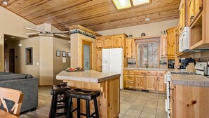 A kitchen with wooden cabinets, a central island with stools, and a refrigerator. - * Snowy Evening Lodge * / Treetop Views & Firepit (Big Bear)
