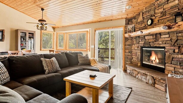 A cozy living room with a stone fireplace, wooden ceiling, and a large sofa. - * Snowy Evening Lodge * / Treetop Views & Firepit (Big Bear)