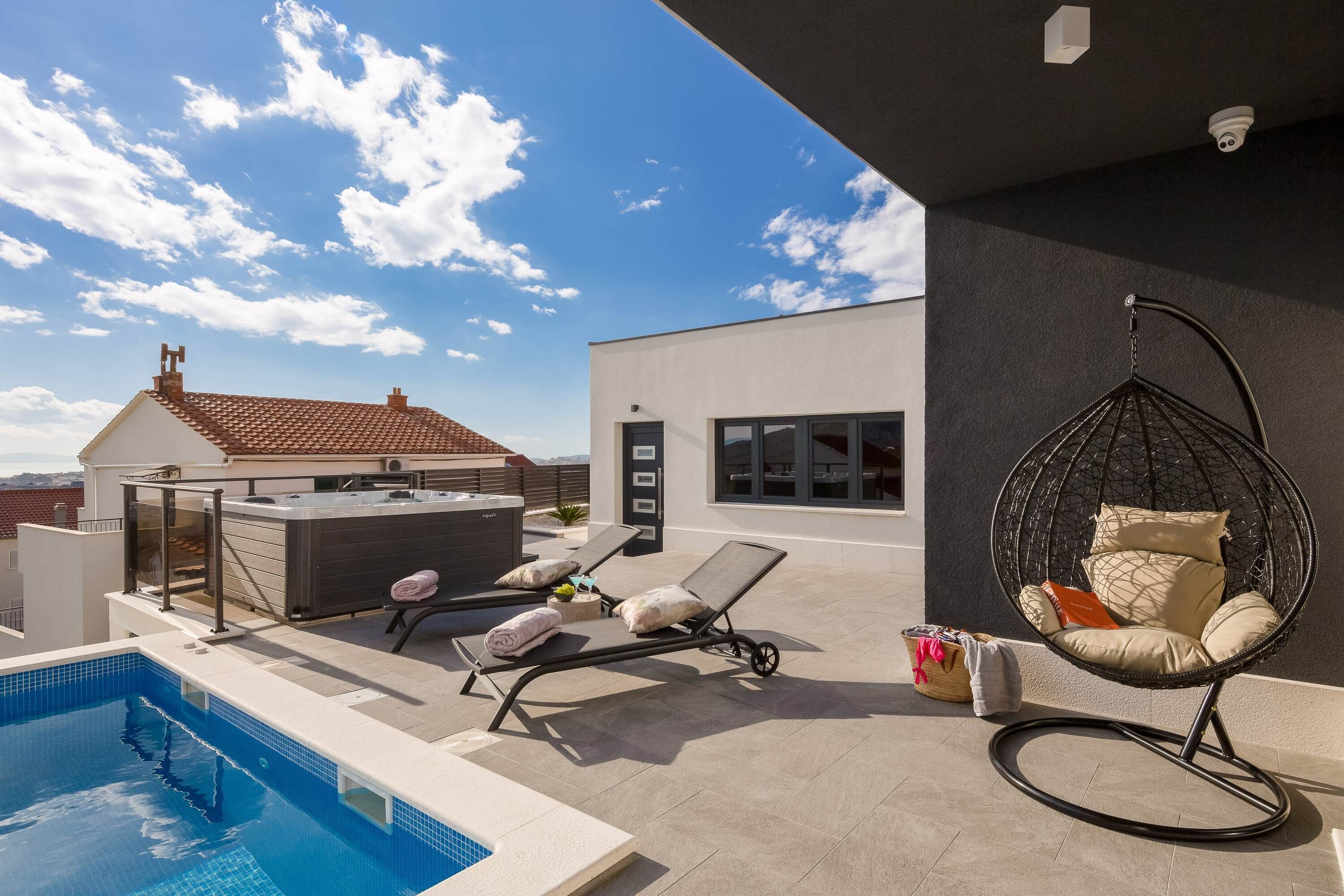 Un espace piscine aménagé sur le toit, avec un fauteuil suspendu, des chaises longues et un jacuzzi.