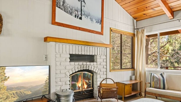 A cozy living room with a fireplace, a television, and a large window offering a view of the outdoors.