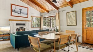 A cozy living room with a fireplace, a dining table with chairs, and a sofa.