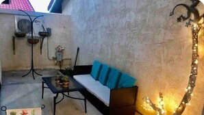 Un espace extérieur accueillant avec un canapé et une table, un tableau représentant un cactus et un arbre décoratif illuminé.