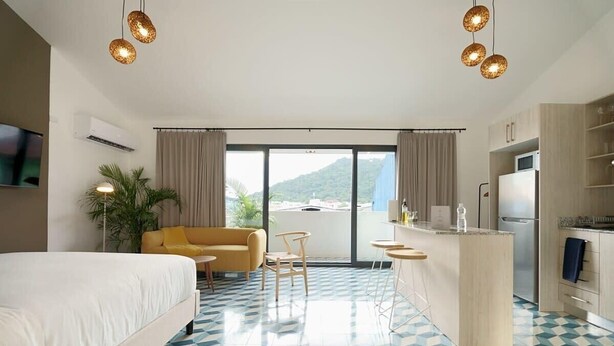 A hotel room with a bed, a sofa, a dining area, and a kitchen.