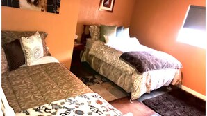 A room with two beds, patterned bedding, a small rug, and a framed picture on the wall. - Quail Befroom  (La Quinta)