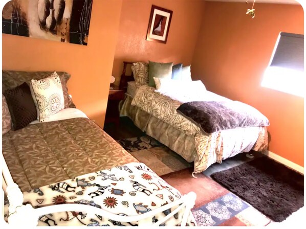 A room with two beds, patterned bedding, a small rug, and a framed picture on the wall.