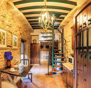 A rustic kitchen with stone walls, a wooden staircase, and a chandelier.