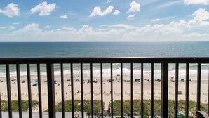 A beach view from a balcony with a railing, sandy beach, and ocean.