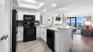 A modern kitchen with white cabinets, a black refrigerator, and a microwave. There is a skylight above the kitchen, and a balcony with a view.