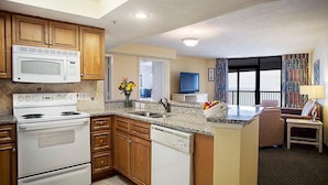A kitchen with wooden cabinets, a microwave, stove, and dishwasher. There is a dining area with a table and chairs, and a view of the outdoors through a large window.