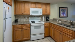 A kitchen with wooden cabinets, a white stove, a microwave, granite countertops, and a sink. - Brilliant Oceanfront 12th Floor 3BR Condo (Myrtle Beach)