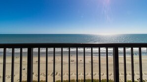A beach view from a balcony with a railing, clear sky, and sunlight reflecting on the water. - Brilliant Oceanfront 12th Floor 3BR Condo (Myrtle Beach)