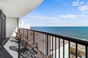 En balkon med udsigt over havet, møbler af træ og et gelænder.