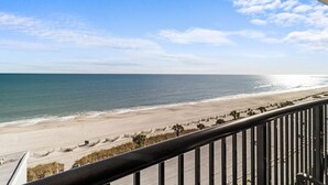 Vista de la playa desde un balcón con barandilla, océano y cielo despejado.