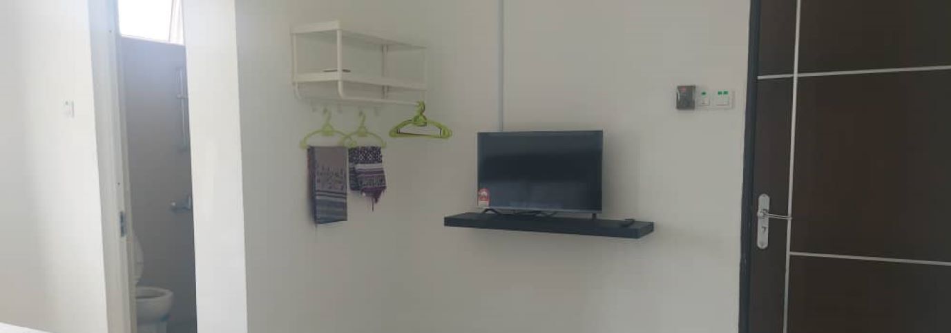 A room with a mounted TV on the wall, a white shelf above it, and a door with a handle.