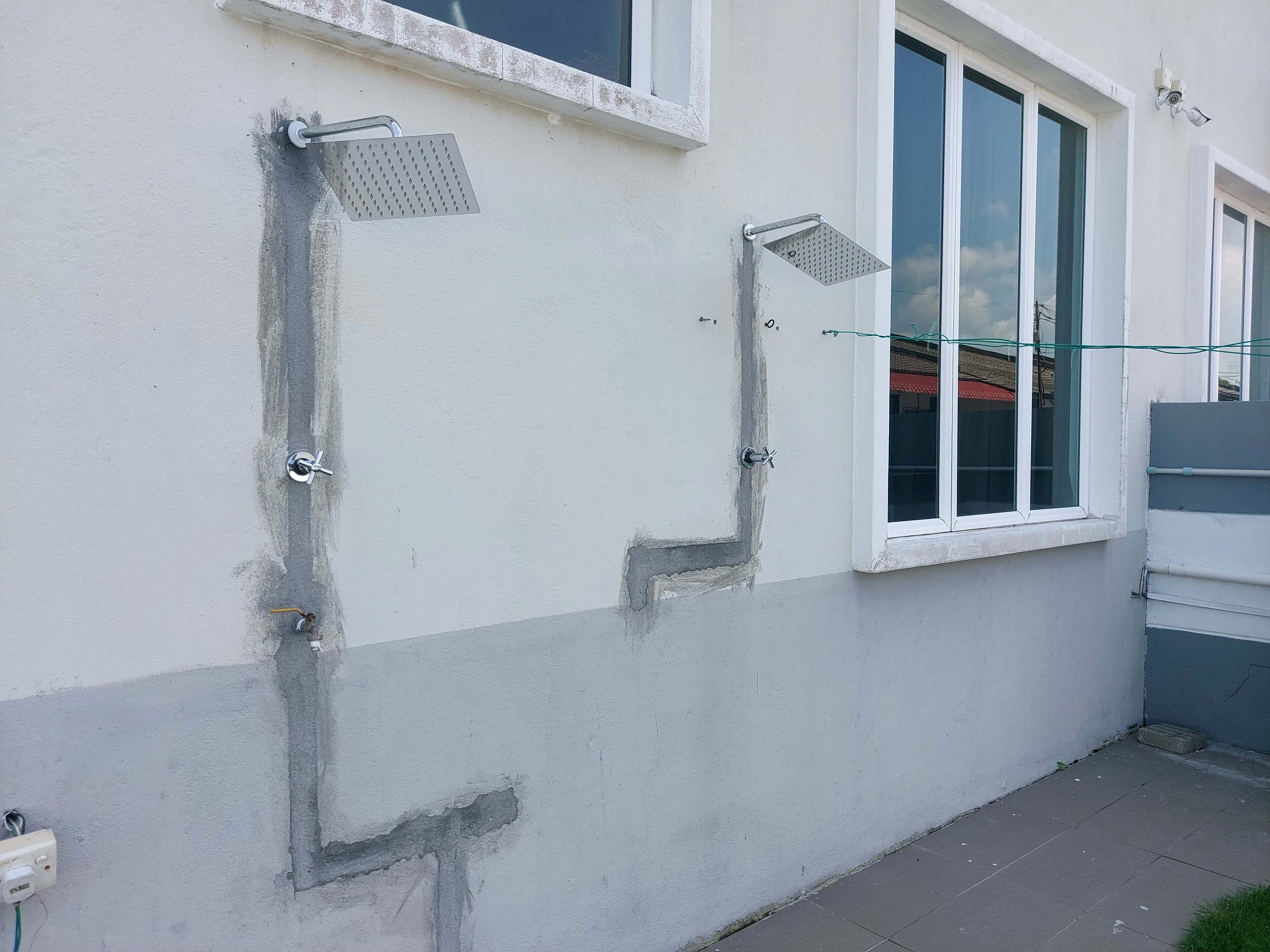 Une façade d’immeuble avec une fenêtre, une gouttière en métal et une boîte électrique visible.