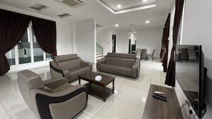 A modern living room with two sofas, a coffee table, and a TV. There is a dining area in the background with a table and chairs. - Alpine PD Taman Kiara 2 Homestay (Port Dickson)