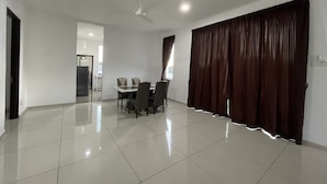 A spacious room with a dining table and chairs, a ceiling fan, and a large window with curtains. - Alpine PD Taman Kiara 2 Homestay (Port Dickson)