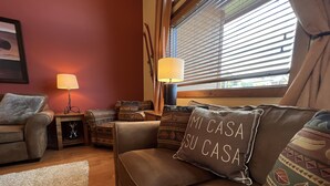 Una sala de estar acogedora con un sofá marrón, cojines estampados y una lámpara.