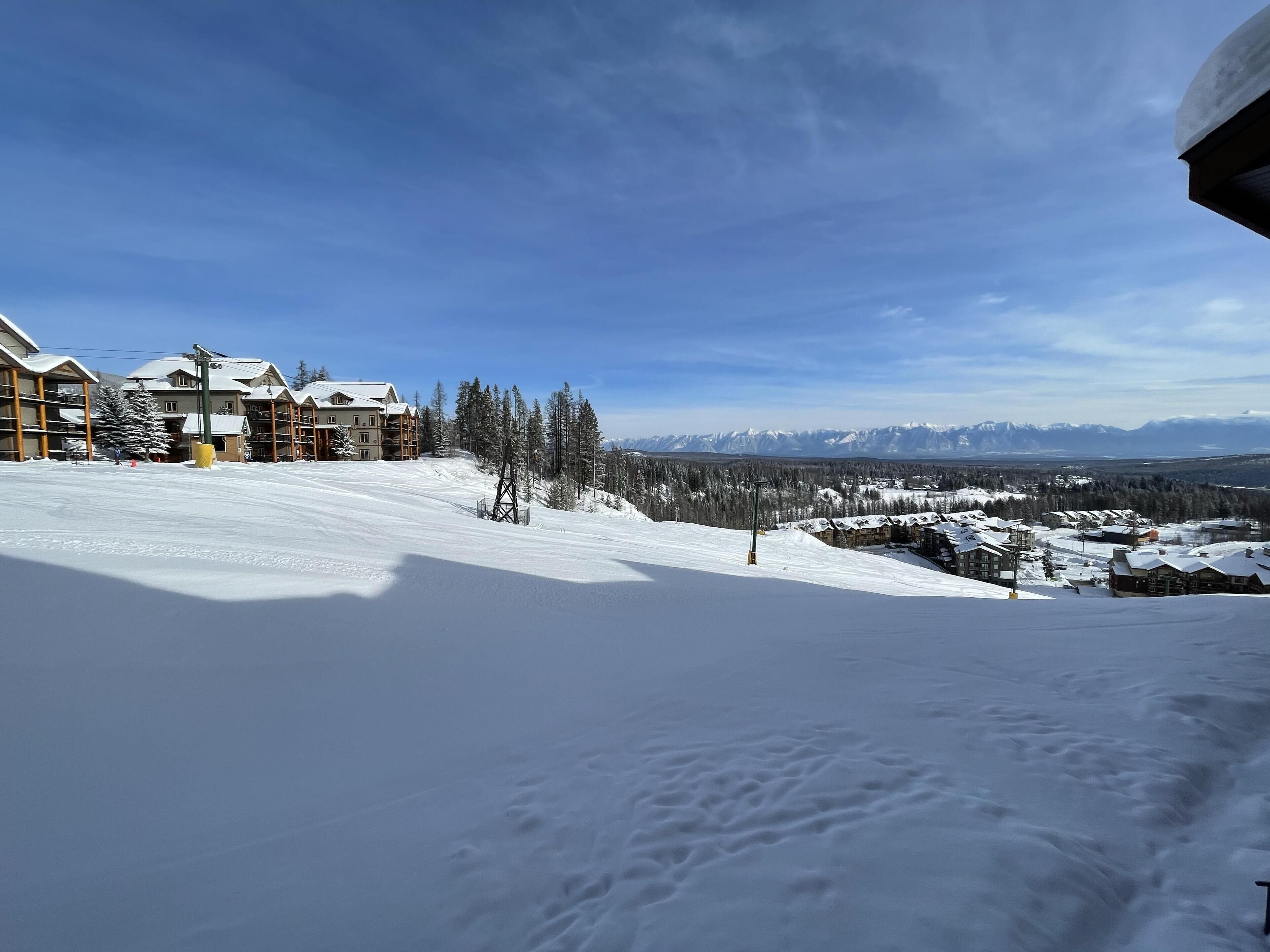 Une piste de ski enneigée, avec des bâtiments et des arbres en arrière-plan.