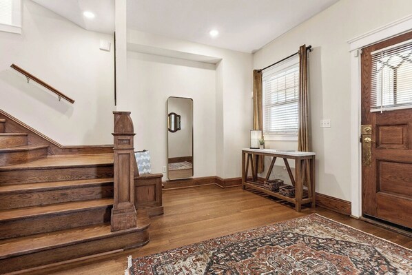 A staircase with wooden steps and a handrail, a mirror on the wall, a console table with a lamp, and a patterned rug on the floor.