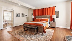 Ein Schlafzimmer mit einem hölzernen Bett, orangefarbenen Vorhängen, einer Bank und einem gemusterten Teppich.