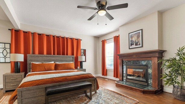 Ein Schlafzimmer mit einem Bett, einer Bank, einem Kamin, einem Deckenventilator und einem Fenster mit Vorhängen.