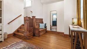 A staircase with wooden railings and a bench, leading to a room with a mirror and a table with a lamp. - The Pioneer - Charming Home Walkable to Streetcar! (Kansas City)