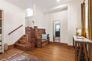 Una escalera con barandas de madera y un banco, que conduce a una habitación con un espejo y una mesa con una lámpara.