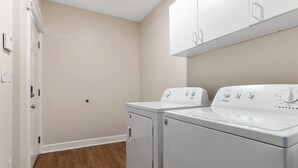 A laundry room with two white Whirlpool washers and dryers, a wooden floor, and a white door. - The Pioneer - Charming Home Walkable to Streetcar! (Kansas City)