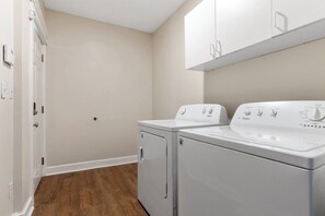 Un lavadero con dos lavadoras y secadoras Whirlpool blancas, suelo de madera y una puerta blanca.